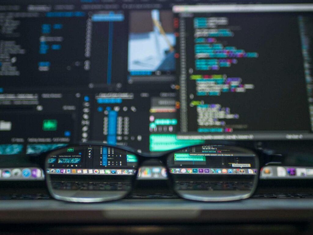 Az olvasószemüveg a laptop billentyűzetén ül, és a több kódoló ablakot megjelenítő képernyőre összpontosít. A szöveg élesen jelenik meg a lencséken keresztül, javítva a programozási környezetet és biztosítva, hogy a WordPress oldalunk megfeleljen a Core Web Vitals szabványoknak.